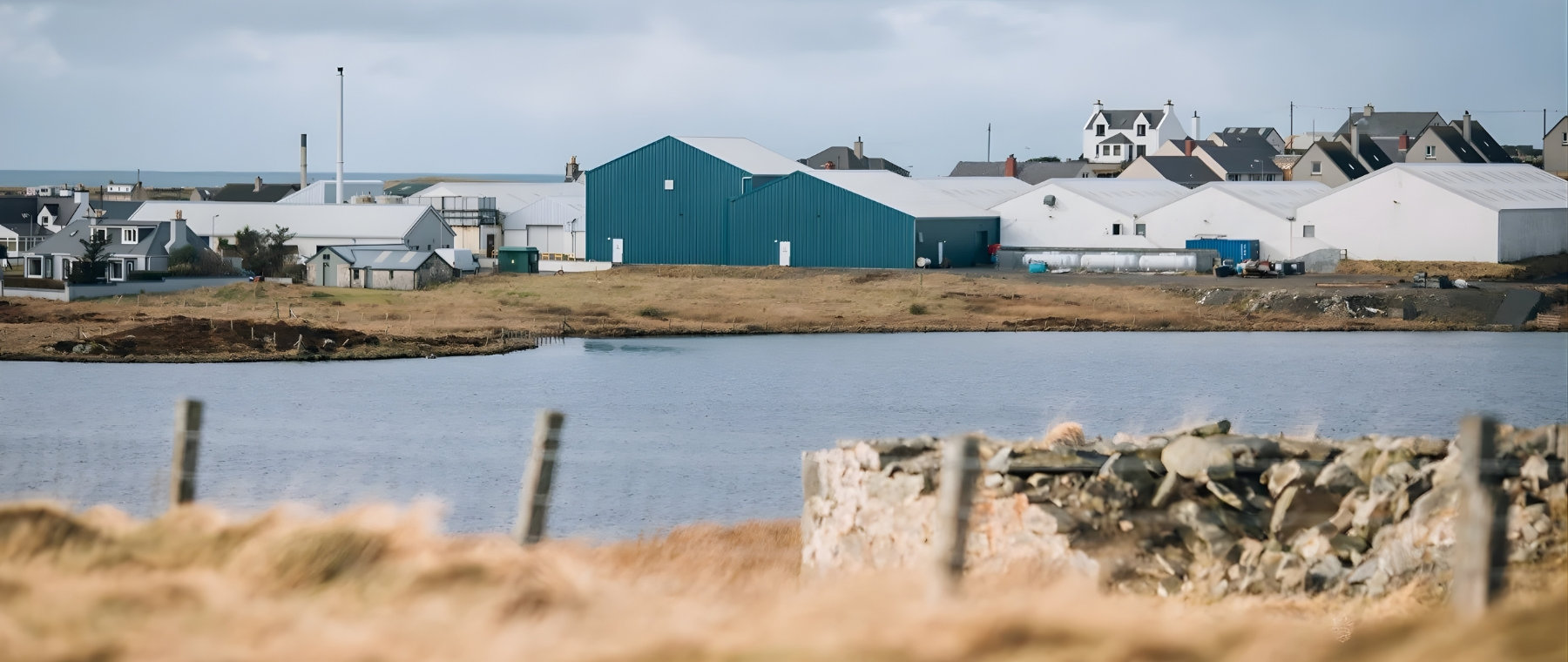 View of Harris Tweed production buildings and village homes across water in the Outer Hebrides