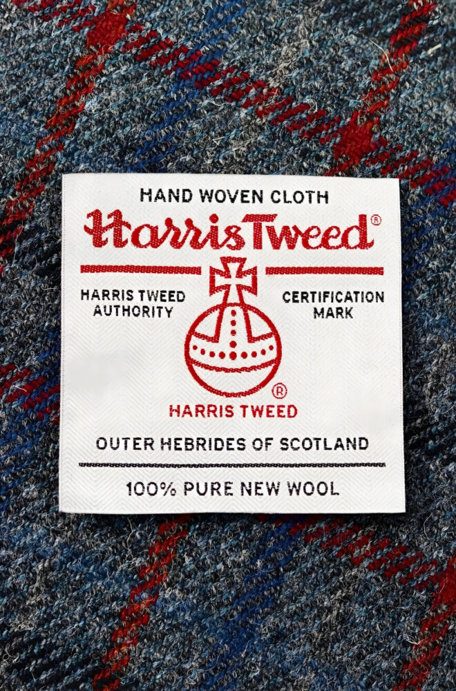 Close-up of Harris Tweed certification label sewn onto blue and red tartan wool fabric